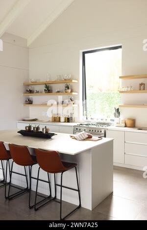 Modern kitchen with white cabinets, island, open shelves, and ample natural light. Stock Photo