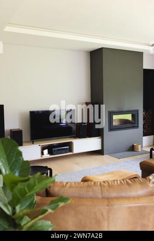 A modern living room features flat-screen tv, a fireplace, and a brown leather sofa Stock Photo