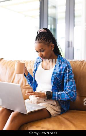 A young African American woman works on her laptop while holding a mug, with copy space Stock Photo