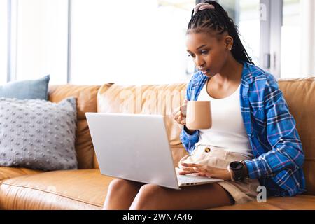 A young African American woman works on her laptop while sipping coffee, with copy space Stock Photo