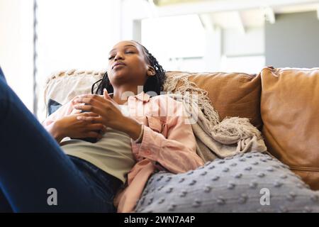 A young African American woman relaxes on a couch, eyes closed and hands clasped Stock Photo