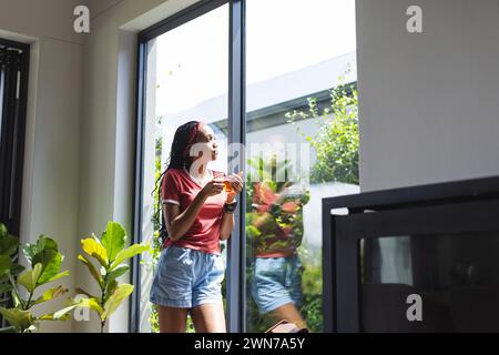 A young African American woman enjoys a slice of pizza by a sunny window Stock Photo