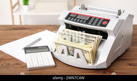 Modern cash counting machine with dollar banknotes, calculator and notebook on table in office Stock Photo