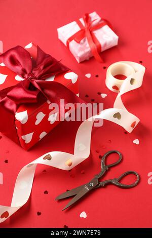 Beautiful gift boxes with ribbon, scissors and confetti on red background. Valentines Day celebration Stock Photo
