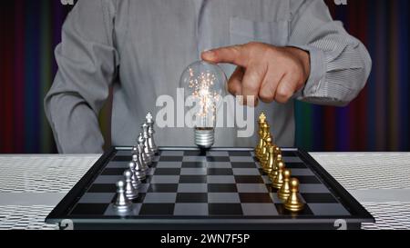 worker touching light bulb on chess board with golden and silver chess pieces Stock Photo