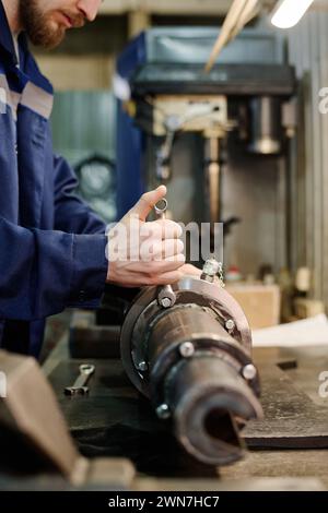 Unrecognizable bearded man repairing metal machine part in workshop, vertical crop shot Stock Photo