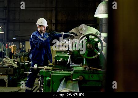 Long shot of young Caucasian man working in factory using lather, copy space Stock Photo
