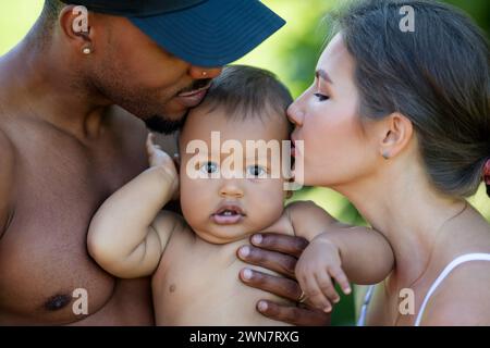 Mothers and father kissed Biracial baby. kissing baby. Mother kiss child, father caring baby. Closeup face of multiracial couple kissing Biracial baby Stock Photo