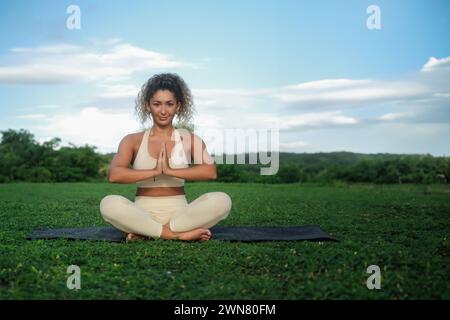 A young Latino woman sits in the lotus position and meditation on the green park Stock Photo