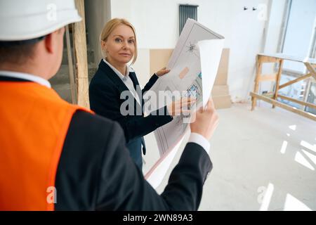 Woman and engineer standing and holding building plan in hands Stock Photo