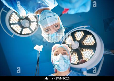 Doctors surgeons in operating room looking at patient under bright lamps Stock Photo