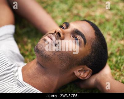 African man, thinking and relax on grass in nature, idea and vision on summer holiday plan. Thoughtful, enjoying fresh air or reflection, sunshine and Stock Photo