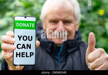 Elder man shows a mobile phone with the test 'donate, you can help'. Stock Photo