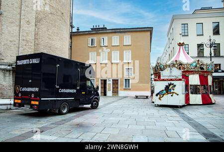 In Parma, a Carabinieri horse transport van parks by a carousel with toy horses, blending tradition with whimsy Stock Photo