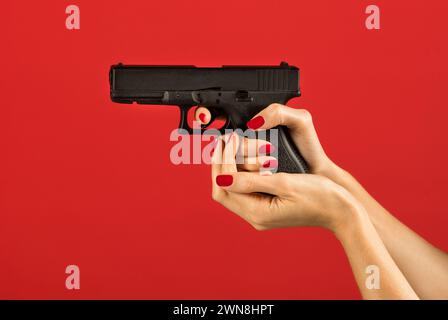 Unrecognizable slim woman holding pistol grip in right hand while keeping index finger with nail polish on trigger and supporting magazine chamber wit Stock Photo