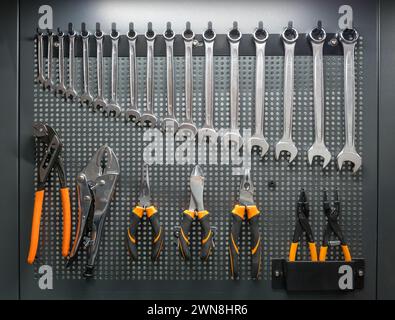 Set of spanners and pliers commonly used by mechanics for maintenance of engines hanging on tool board in workshop Stock Photo