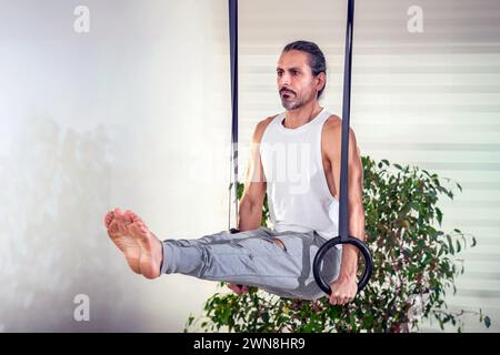 Adult man doing L Sit exercise with rings against potted plant at home during fitness workout Stock Photo