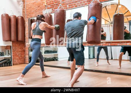 Back view of concentrated anonymous male and female in barefoot and in sportswear looking away while standing on gym floor in boxing gloves and punchi Stock Photo