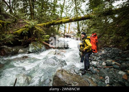 Backpacker carrying gear looks for a river crossing location Stock Photo