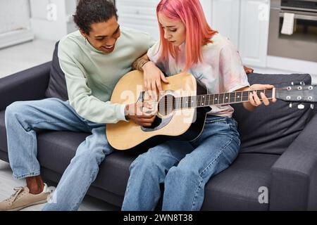 handsome jolly african american man teaching his girlfriend how to play guitar while at home Stock Photo