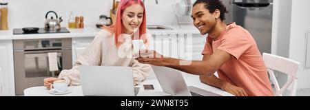 joyous multicultural couple in cozy homewear looking at smartphone while working remotely at home Stock Photo