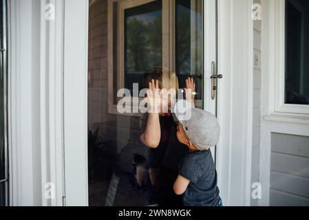 Two boys make faces at each other through a glass window. Stock Photo