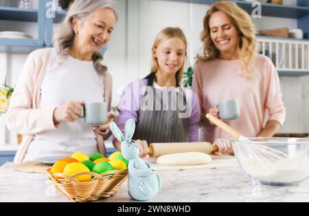 Three generations unite in kitchen, mother, grandmother, and granddaughter, as they preparing for Easter with love and laughter. Basket with painted e Stock Photo