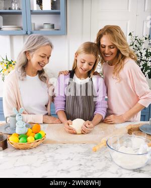 Happy three generations of women preparing Easter dishes in beautiful kitchen, kneading dough, coloring eggs, and preparing for celebration of Easter Stock Photo