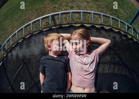 Overhead view of boy and girl talking while laying on trampoline. Stock Photo