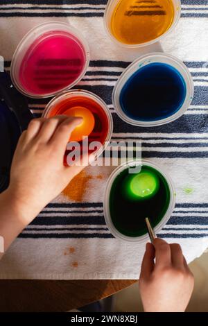 Child reaching into food coloring to pick up Easter egg Stock Photo