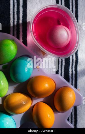 Close up of egg in cup of pink food coloring on striped dish towel Stock Photo