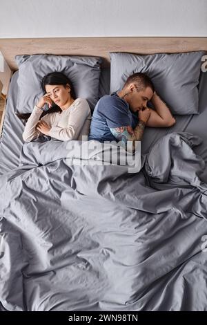 high angle view of depressed interracial couple lying down on bed at home, family divorce concept Stock Photo