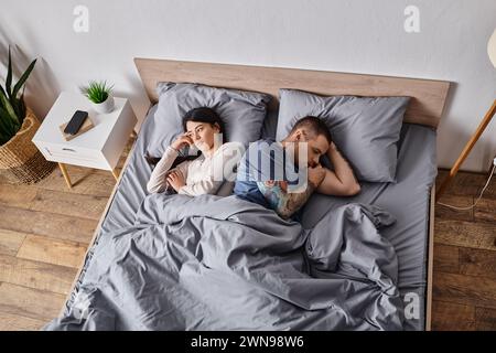 high angle view of upset multiethnic couple lying down on bed at home, family divorce concept Stock Photo