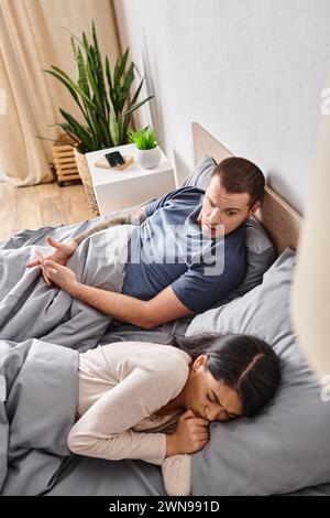 high angle view of angry man quarreling at offended asian wife on bed at home, divorce concept Stock Photo