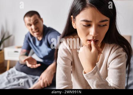 young frustrated asian woman sitting near angry husband in quarrelling in bedroom, divorce concept Stock Photo
