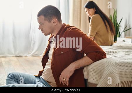 young  frustrated man sitting on floor near upset asian wife, relationship difficulties concept Stock Photo