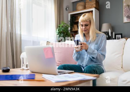 Young business woman freelance expatriate in smart casual working at home in home office using smartphone to check questions on email preparation for Stock Photo