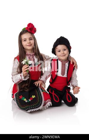 Bulgarian girl and boy in ethnic folklore costumes with spring traditional martenitsa on hands and bouquet of snowdrops,happy Baba Marta day, Bulgaria Stock Photo
