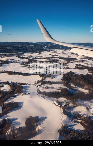 Airplane flying low over snowy mountains and preparing for landing to the airport, view from plane window of wing turbine and skyline Stock Photo