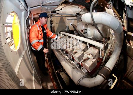 01 March 2024, Saxony-Anhalt, Halberstadt: Michael Brandes from VIS Halberstadt inspects the engine in the SVT machine car. The GDR prestige train SVT is slowly placed on the chassis using a lifting platform. After this step, the further refurbishment of the SVT can continue. Under the watchful eyes of numerous guests, the VT 18.16.10 engine car was lifted to approx. 2.60 meters in the VIS Halberstadt railroad depot using four lifting jacks, then the bogies were positioned exactly under the vehicle. Finally, the vehicle is slowly lowered until it stands on its own wheels again. The train shoul Stock Photo