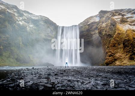 A woman stands in front of a majestic waterfall. Iceland Stock Photo