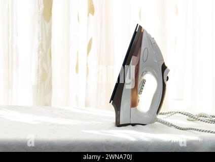 White iron on an Ironing Board against a window background Stock Photo