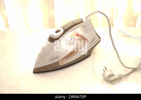 White iron on an Ironing Board against a window background Stock Photo