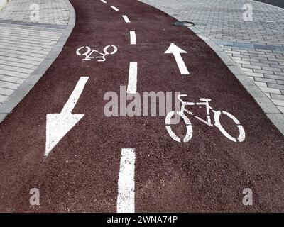 Bike lane with painted white bicycle sign or symbol and arrows on the ground for directions on new black tarmac road. Stock Photo