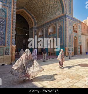 Woman with her chador flowing in the wind walks to the entrance of the Jameh Mosque of Yazd, 14th-century Shia mosque in the Old Town of Yazd, Iran. Stock Photo