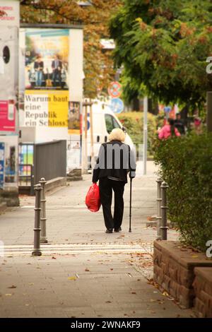 A stylish elderly woman in a black jacket strolls with a red bag in an urban setting Stock Photo