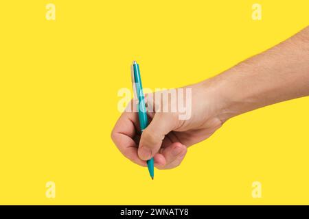 Hand with Green Ballpoint Pen on Yellow. Represents productivity, great for showcasing writing skills or office products. Stock Photo