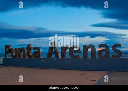 Evening light on the metal Punta Arenas sign near the shore. The sign commemorates 500 years since the discovery of the Strait of Magellan. Stock Photo