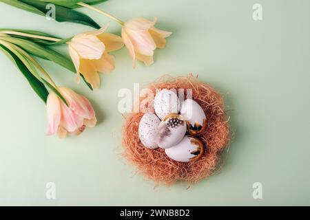 Nest with Easter eggs and yellow tulips on light green background. Easter concept. Top view, flat lay. Stock Photo