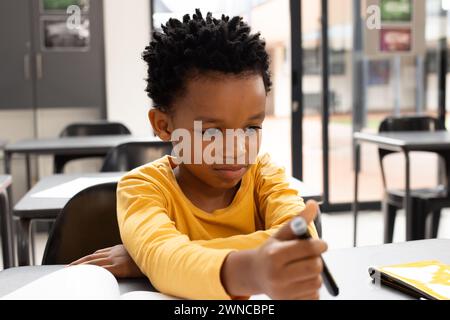 African American boy with short curly hair is focused on drawing in a school classroom Stock Photo